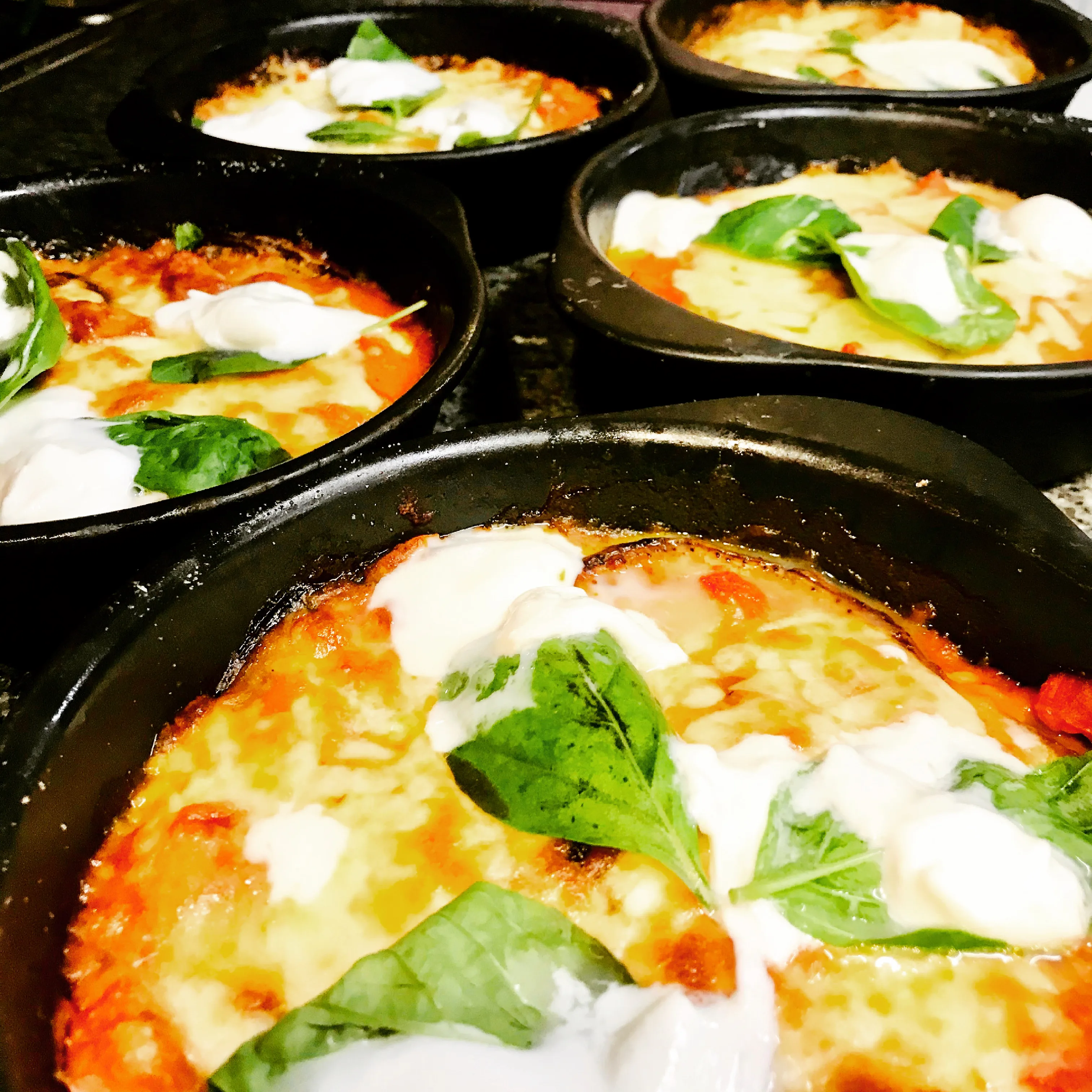 Quatre cocottes de melanzana alla parmigiana gratinées, mozzarella fondue et basilic, à la sortie du four.