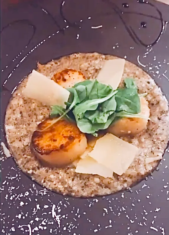 Risotto aux noix de Saint-Jacques snackées, copeaux de parmesan et jeunes pousses, sur assiette d'ardoise.